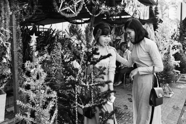 14 Dec 1967, Saigon, South Vietnam --- Saigon: Christmas Shopping. War worries seem forgotten as these two Vietnam girls shop for a Christmas tree in Saigon. Holiday is only ten days off. --- Image by © Bettmann/CORBIS