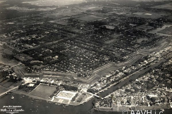 http://www.aavh.org/?p=1922

Hué, 1932  La Citadelle  Vue aérienne

Notice : Sur la Citadelle de Hué, voir AP0032. Vue aérienne de la citadelle prise de langle sud-est. De g. à d. on aperçoit au premier plan : le pont Clemenceau ; le marché de Dong Ba ; le canal de Dong Ba que franchit un pont avec, sur la rive gauche, le quartier de Dong Ba, et, sur la rive droite, celui de Gia Hoi. En arrière, les douves et les remparts de langle sud-est de la citadelle. Sur les bâtiments de la Cité Impériale, voir AP1923. Notule : Hué  Origine légendaire et emplacement  » Comme dans les contes merveilleux, deux fées ont présidé à la naissance de notre bonne Capitale : ces deux marraines à qui la postérité na pas toujours rendu lhommage quelles méritent, ce sont les princesses Huyen Tran, de la dynastie des Tran, et Ngoc Bau, de la famille des Nguyen. Sous les premières dynasties annamites, Hué avec le territoire dans lequel elle est enclavée, faisait partie de lhinterland cham. Le fleuve Song Gianh servait alors de limite entre lAnnam et le Champa, qui vivaient dans un état de conflit permanent. De longues guerres meurtrières ravageaient périodiquement les deux pays voisins, entrecoupées de courtes trêves. Cest au cours dun de ces répits momentanés que le roi Tran Nhan Ton, désireux détablir une paix durable entre les deux pays, fit un voyage diplomatique au Champa. Bien plus, afin de sceller laccord des deux royaumes par les liens indissolubles de lhymen, il promit au roi cham Che Man, la main de sa fille Huyen Tran. Celui-ci, pour reconnaître lhonneur dune telle alliance, offrit en retour deux districts limitrophes de lAnnam : O et Ly, comprenant le Quang Binh, le Quang Tri, le Thua Thien et le Nord du Quang Nam actuel. Cest ainsi que par une belle matinée de printemps de lannée 1307, la princesse Huyen Tran se mit en route vers le Sud pour la grande aventure. On comprend létat dâme de cette jeune princesse qui avait vécu jusque-là choyée, adulée, à lombr